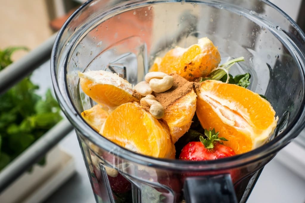 Orange slices, strawberries, and cashews in a blender