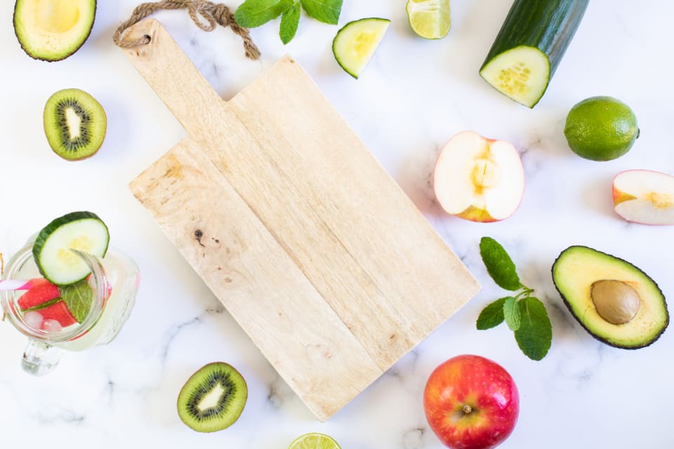 Fresh fruit and vegetables arranged around a wooden cutting board